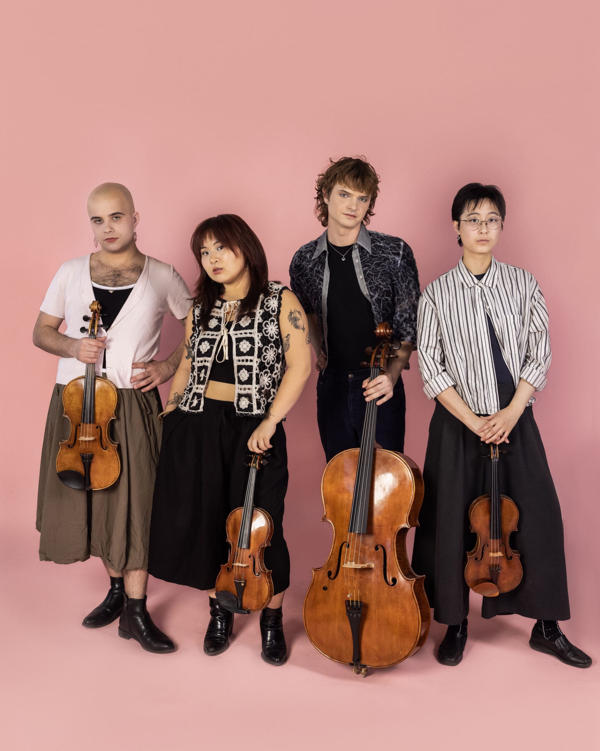 Four musicians pose against a pink backdrop, each holding a string instrument (violin or cello).
